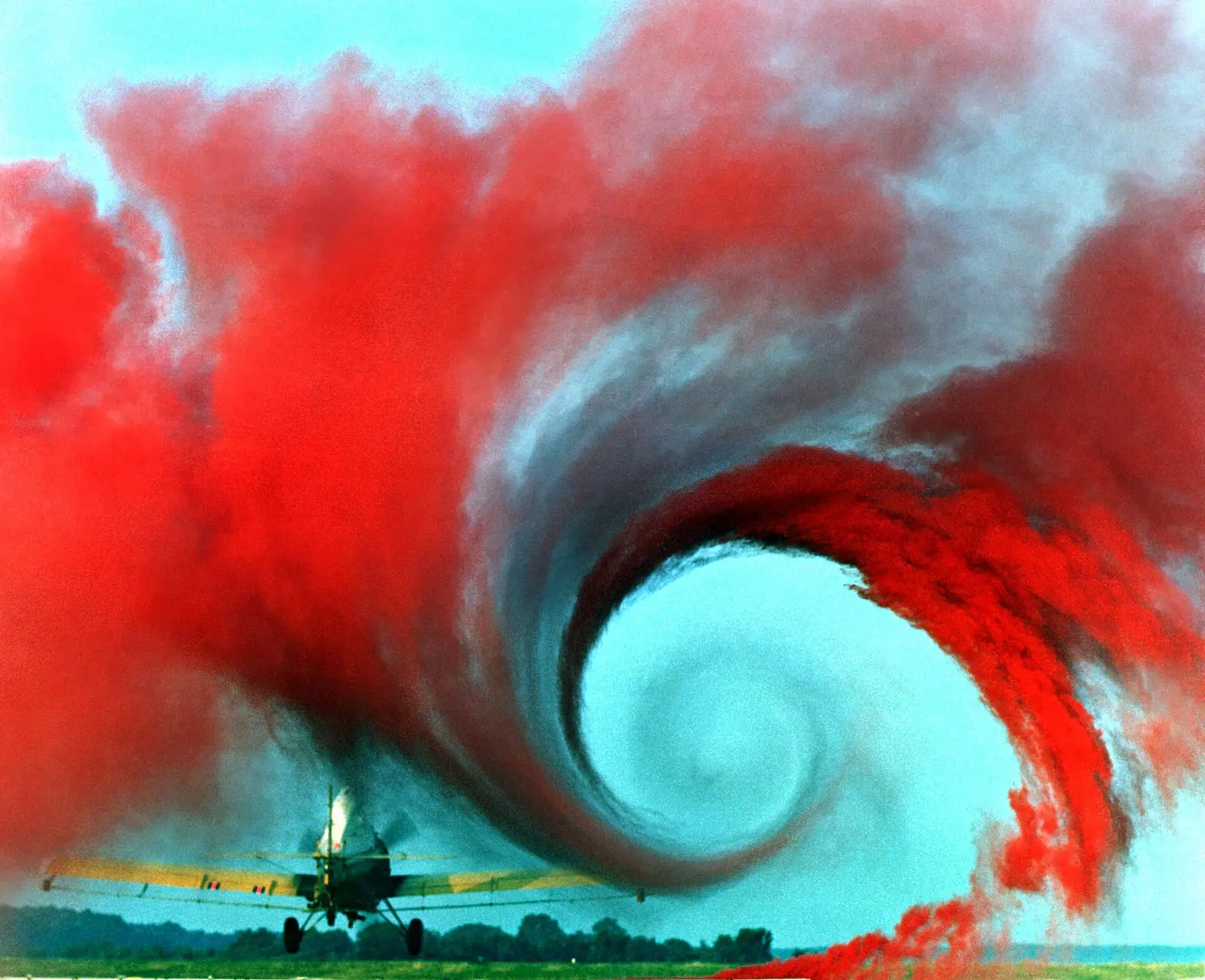 A low-flying crop-duster trailing a huge spiral of red smoke from its wingtip.
