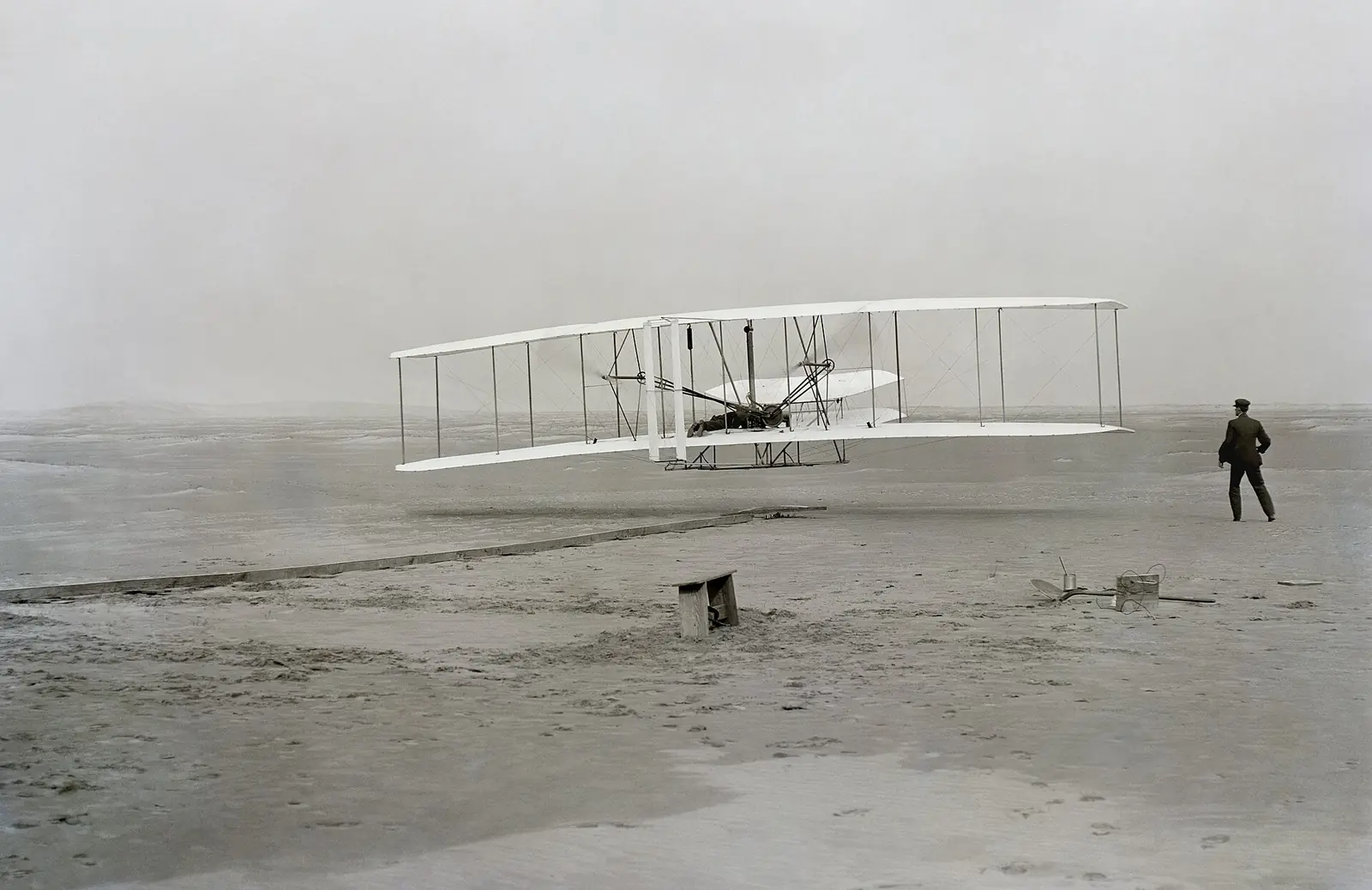 The Wright Flyer a few feet off the sand at Kill Devil Hills, with Wilbur Wright running alongside.